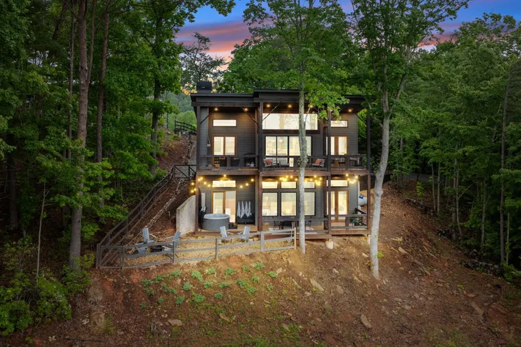 Modern three-storey rental lit up on a wooded hillside at dusk