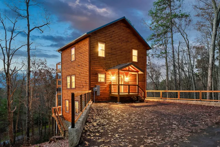 Three-storey log cabin glowing at dusk above a hillside drive